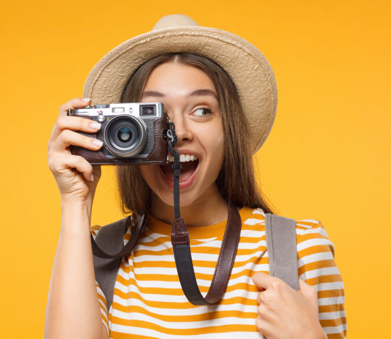 tourism concept. horizontal banner of excited young woman tourist holding photo camera, isolated on yellow background with copy space